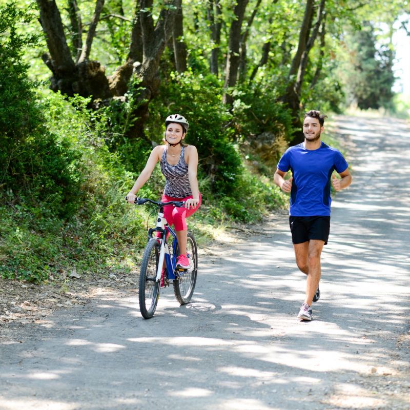 young woman riding bicycle beside a young man running in countryside in summer